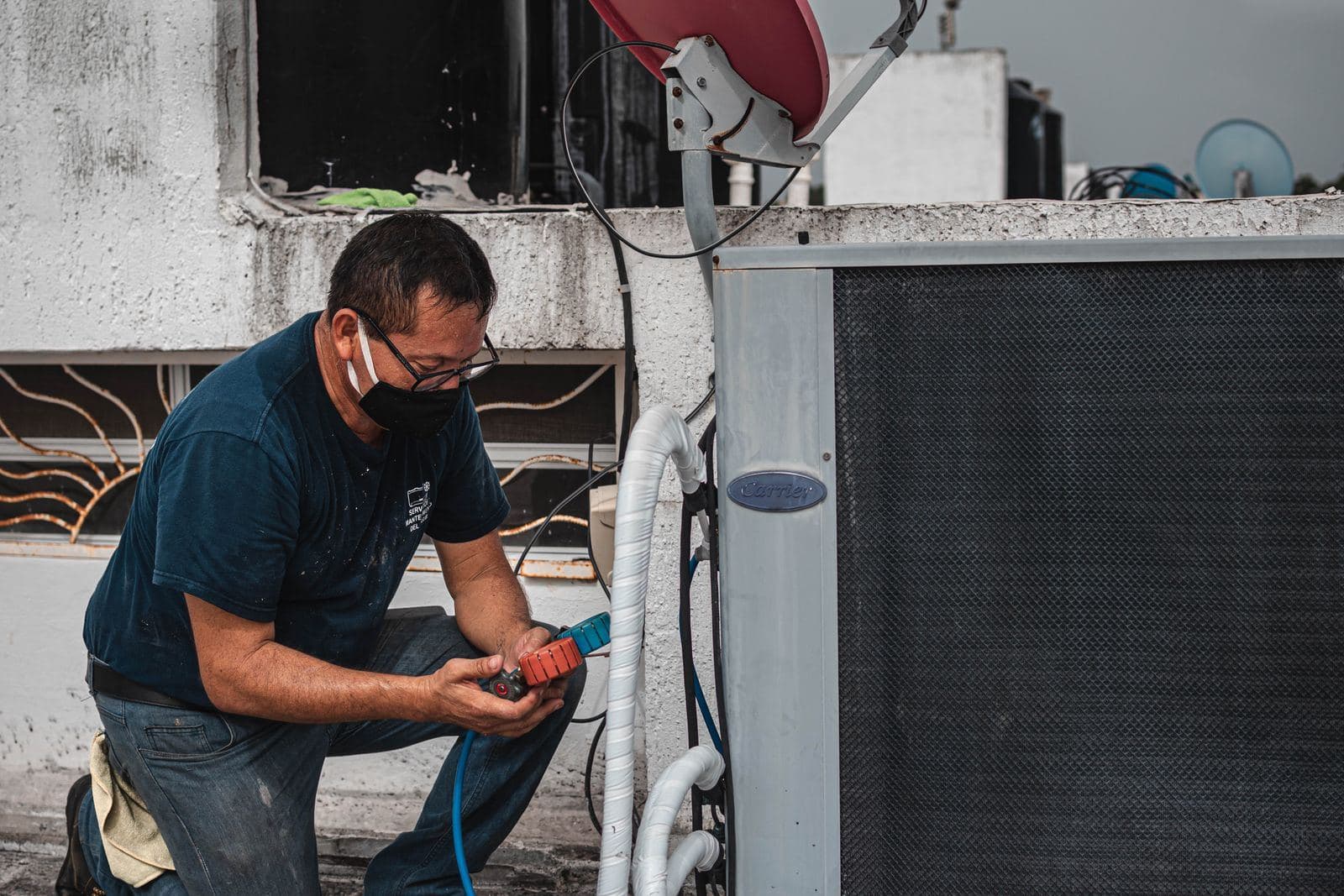 Technician kneeling beside an outdoor AC unit with test equipment